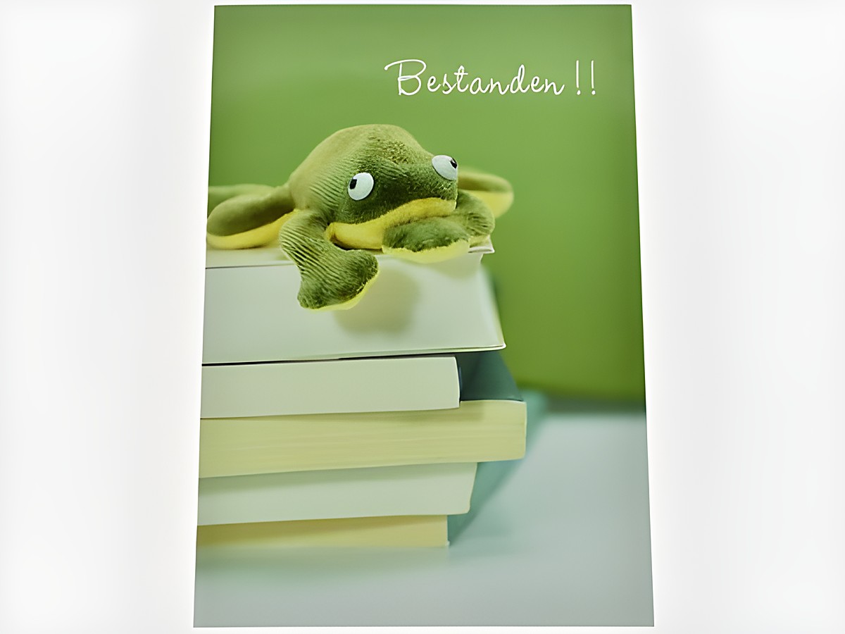Auf der Glückwunschkarte liegt ein Plüschfrosch auf einem Stapel Bücher, im Hintergrund ist eine grüne Fläche zu sehen. Oben auf der Karte steht der Text Bestanden.