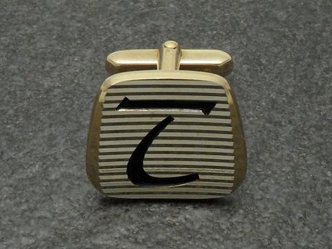 Vergoldete Manschettenknöpfe mit Initialen T, von Juwelier Harnisch, mit gestreiftem Design und schwarzer Schrift. Ideal für elegante Anlässe.