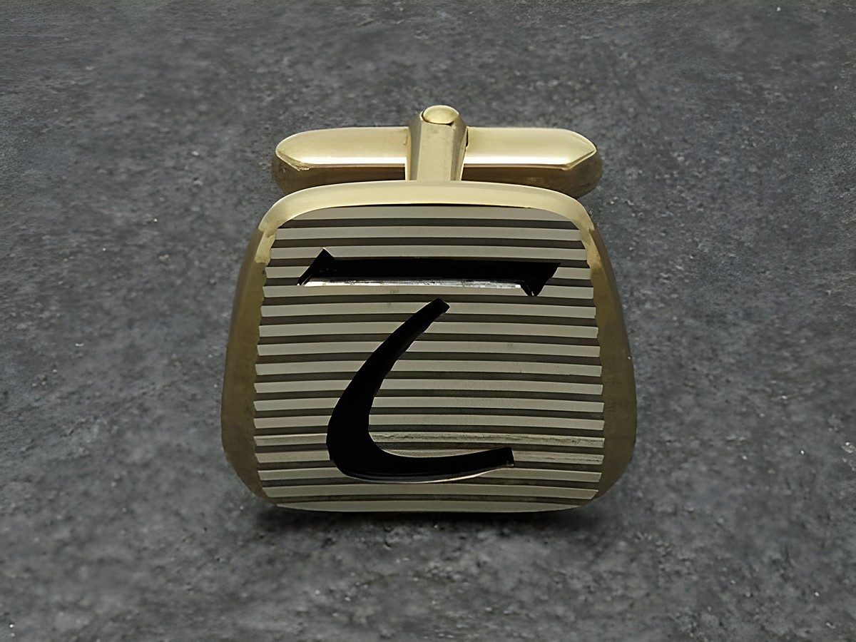 Vergoldete Manschettenknöpfe mit Initialen T, von Juwelier Harnisch, mit gestreiftem Design und schwarzer Schrift. Ideal für elegante Anlässe.