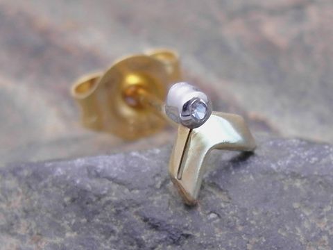 Einstückiger unisex Ohrstecker in bicolor Gold 585 mit symbolischem Design und einem Diamanten, hergestellt von Juwelier Harnisch, auf einem steinernen Hintergrund.
