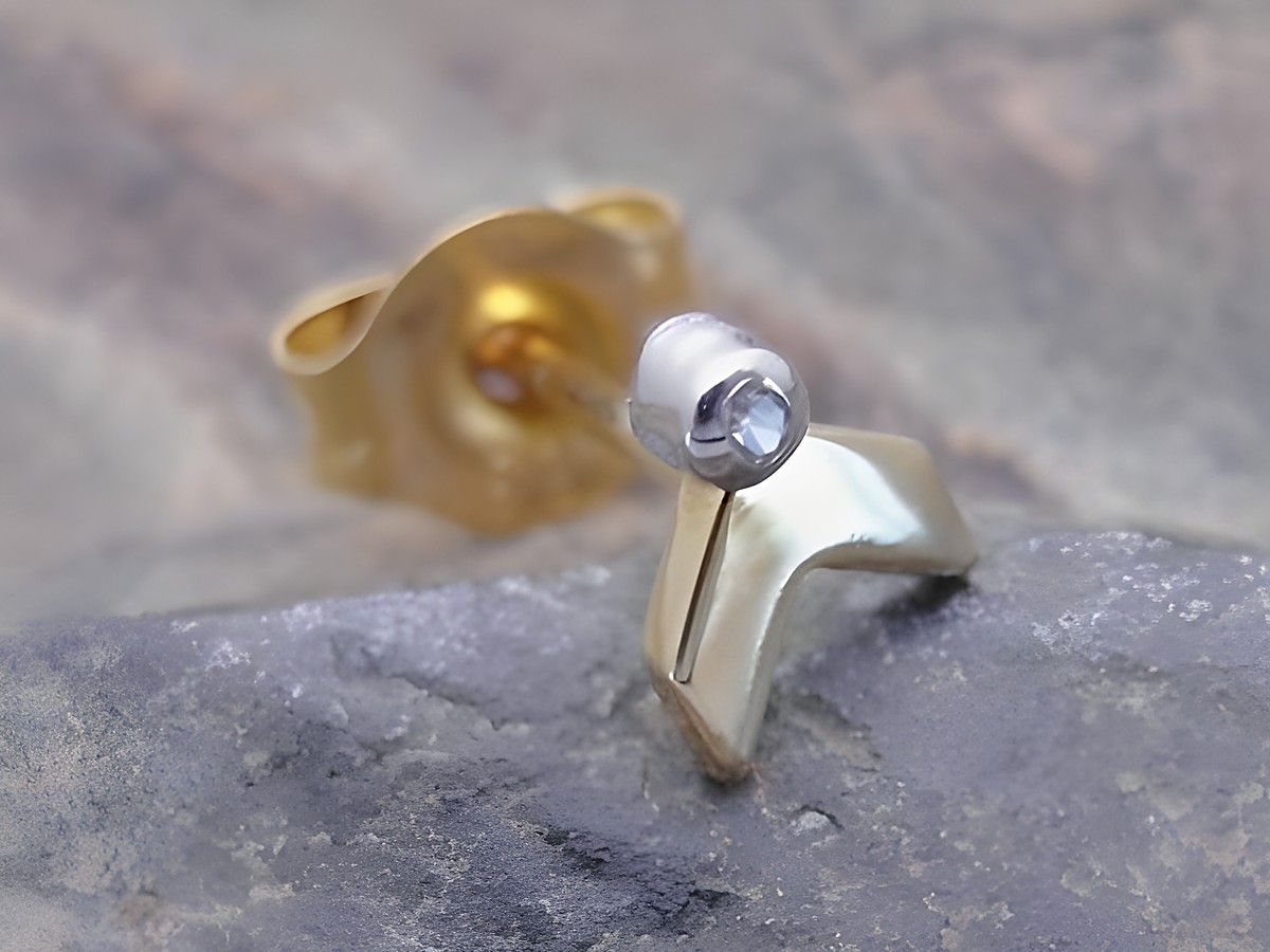 Einstückiger unisex Ohrstecker in bicolor Gold 585 mit symbolischem Design und einem Diamanten, hergestellt von Juwelier Harnisch, auf einem steinernen Hintergrund.