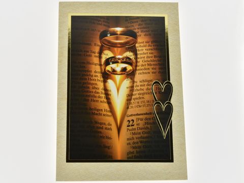 Eine elegante Hochzeitskarte mit goldenen Ringen, die schimmernd auf einer offenen Bibel liegen. Im Hintergrund ist ein Textausschnitt zu sehen, umrahmt von einem herzförmigen Design.