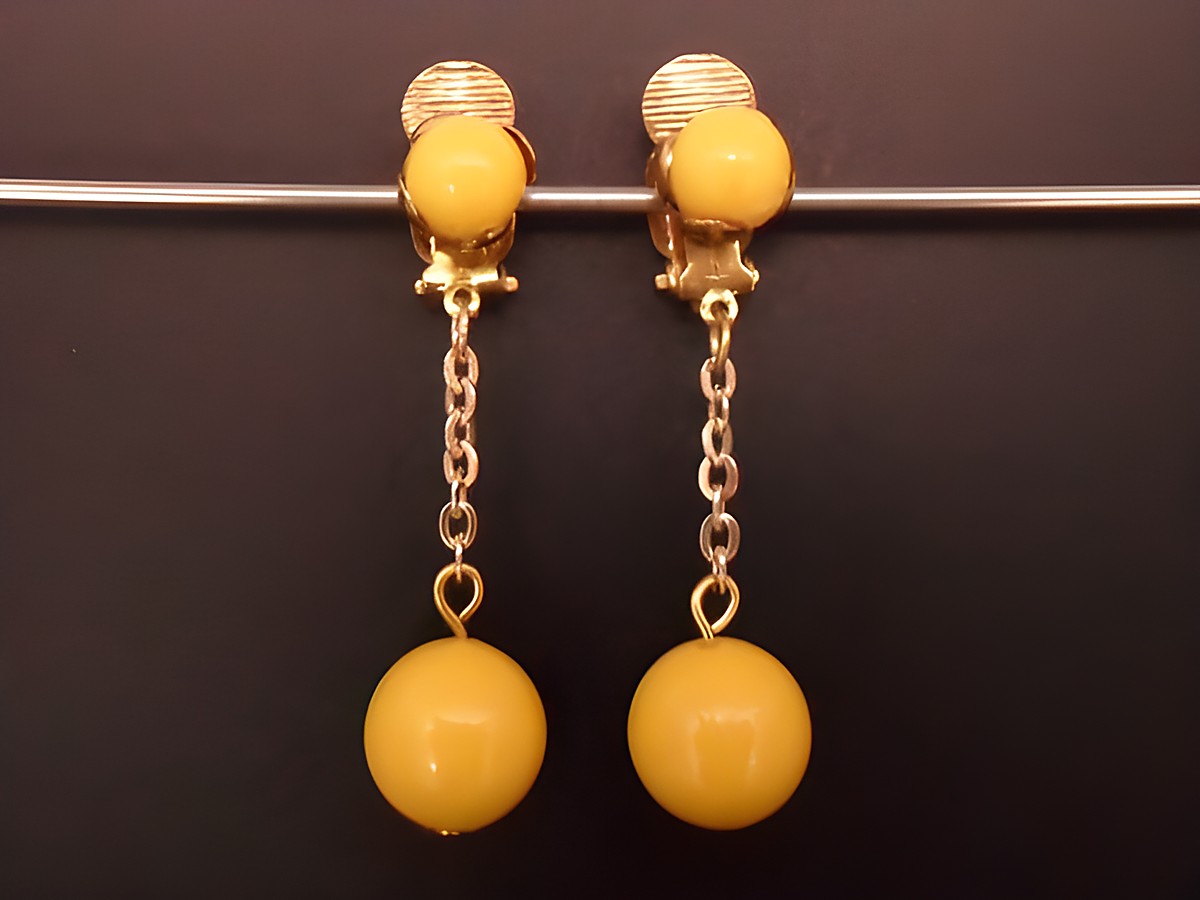 Gelbe zeitlose Ohrclips aus Kunstharz mit goldfarbener Befestigung und einer eleganten Kette, Hersteller Juwelier Harnisch, ideal für jeden Anlass.
