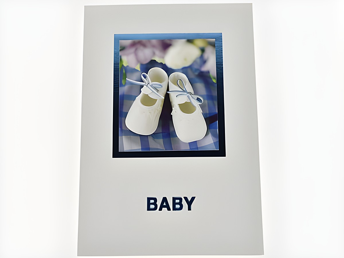 Glückwunschkarte mit Bild von eleganten Babyschuhen in Weiß und blauer Schleife, umgeben von blühenden Motiven, Hersteller Juwelier Harnisch, ideal zur Geburt.