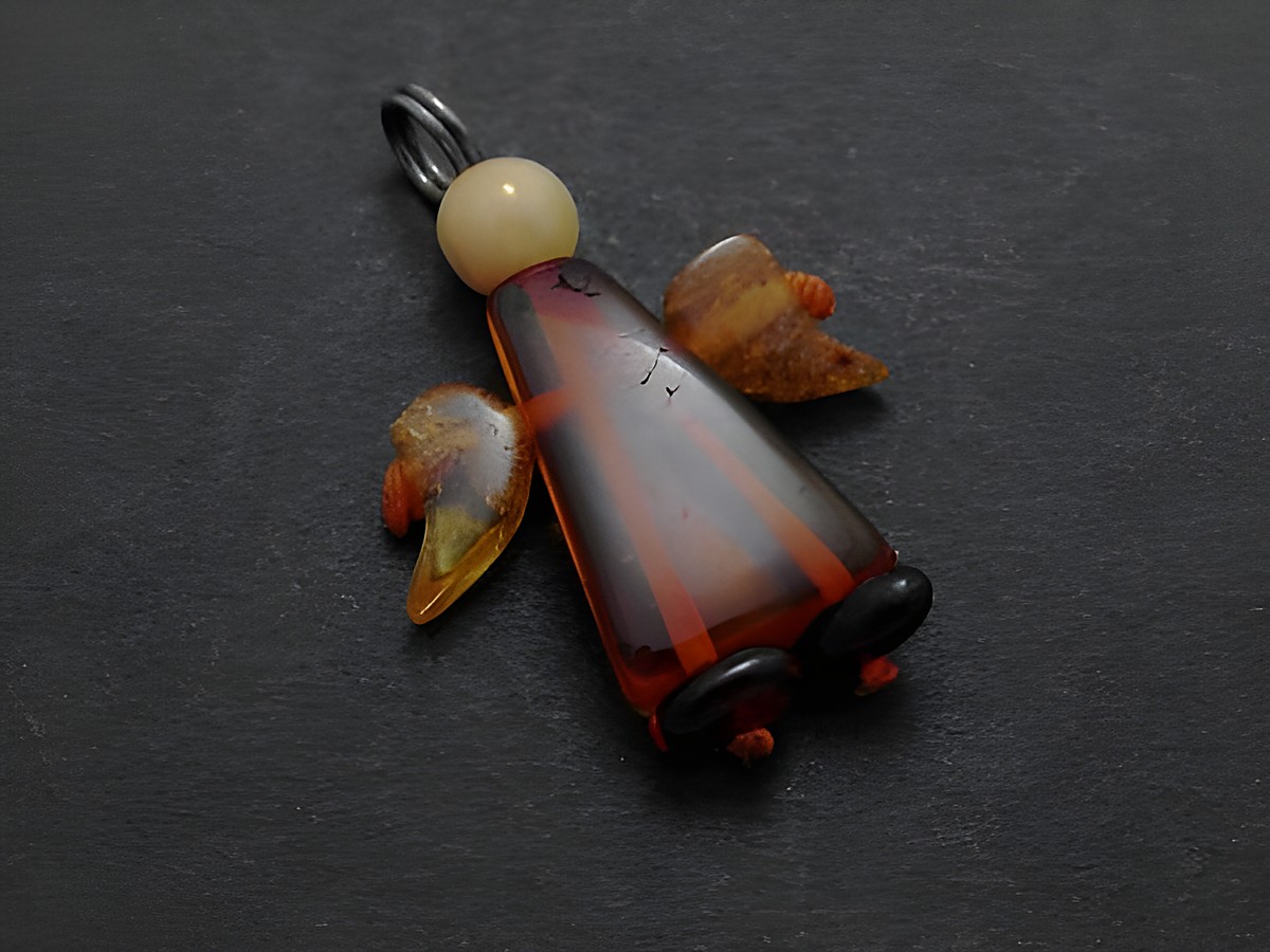 Engel Anhänger aus dunkelbraunem und bernsteinfarbenem Material mit schützenden Flügeln, Hersteller Juwelier Harnisch, idealer Bernstein Schmuck für besondere Anlässe.