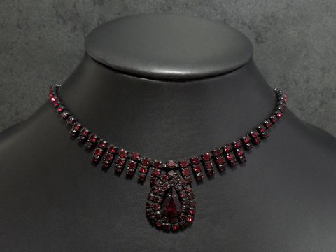 Dunkelrote Strass Kette von Juwelier Harnisch mit einer Fassung in Schwarz, Länge von 45,5 bis 49 cm, geschmückt mit funkelnden Steinen und einem auffälligen Tropfenanhänger.