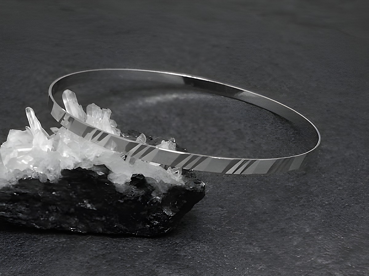 Zarter silberner Armreifen mit einem Durchmesser von 3,4 mm, rhodiniert, misst 21 cm und liegt auf einem schwarzen Untergrund neben transparenten Kristallen. Hersteller Juwelier Harnisch.