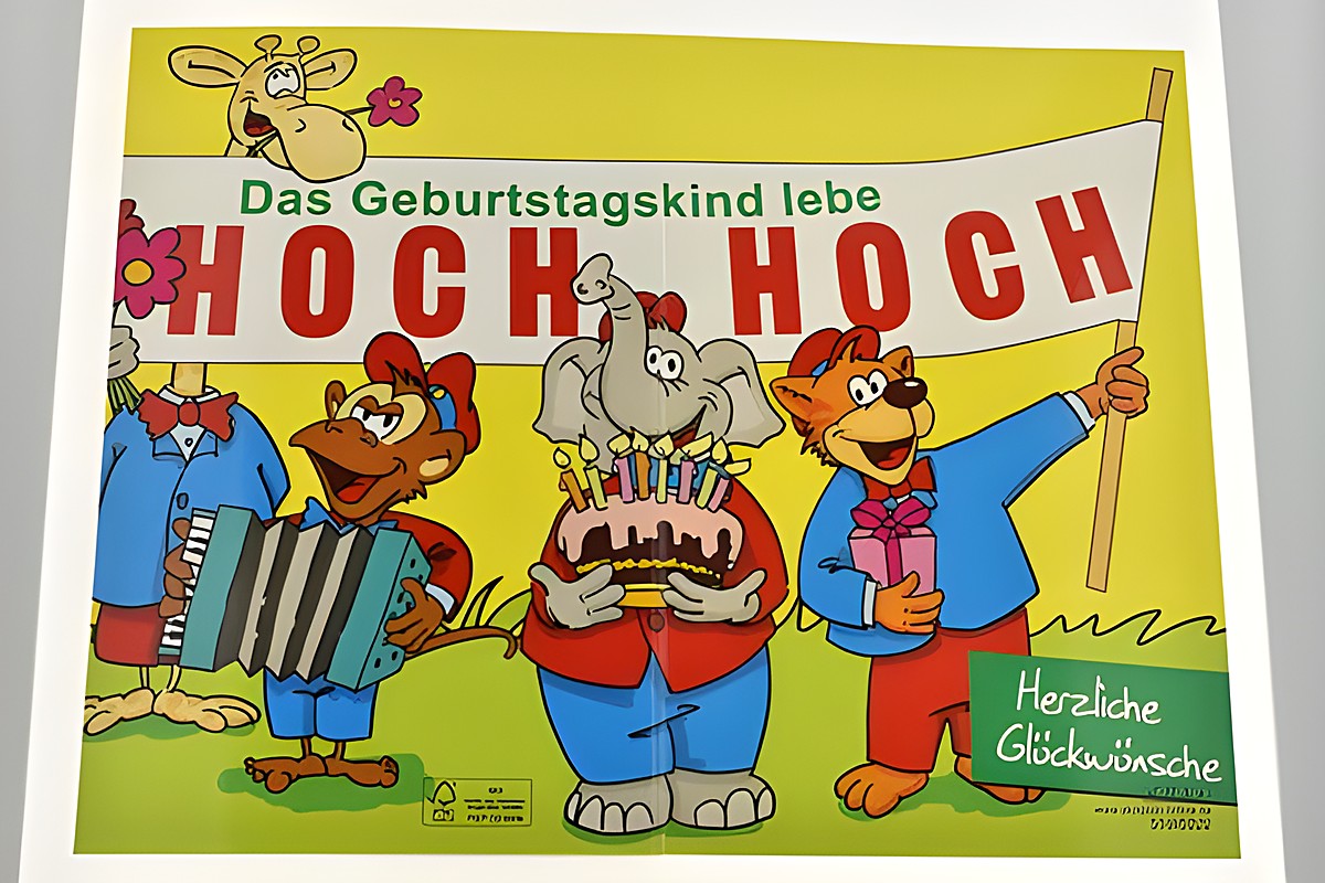 Eine farbenfrohe Geburtstagskarte mit tanzenden Tieren, die ein großes Banner mit Hoch hoch halten. Ein Elefant mit einer Geburtstagstorte und weitere Tiere feiern freudig. Hersteller Juwelier Harnisch. – Ansicht 2