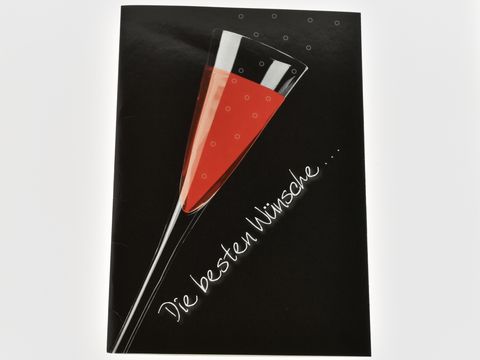Eine Geburtstagskarte mit einem Sektglas, gefüllt mit rotem Inhalt, auf schwarzem Hintergrund. Hersteller ist Juwelier Harnisch. Die Karte enthält den Schriftzug Die besten Wünsche.