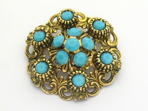 Brosche im Sexy City Look in Türkis, rund mit goldfarbener Verzierung und facettierten Steinen, Hersteller Juwelier Harnisch, idealer Schmuck für stilvolle Akzente.