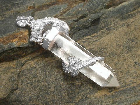Drachen Anhänger aus Silber mit einem Bergkristall Pendel, umschlungen von einem detaillierten Drachenmotiv, hergestellt von Juwelier Harnisch, ein elegantes Schmuckstück mit Edelsteinen.