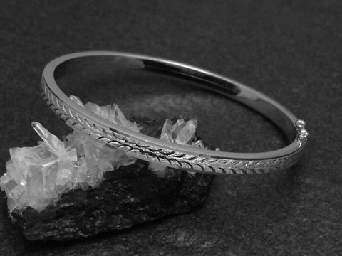 Silber Armreifen mit einem filigranen Muster, 4,8 mm breit, rhodiniert und 18 cm lang, präsentiert auf einem schwarzem Untergrund mit Kristallen. Hersteller Juwelier Harnisch.