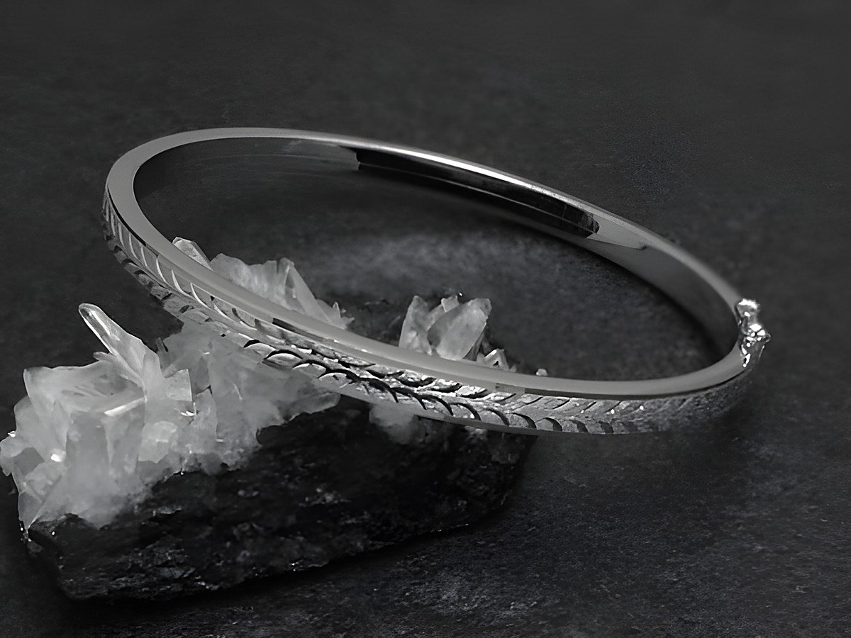 Silber Armreifen mit einem filigranen Muster, 4,8 mm breit, rhodiniert und 18 cm lang, präsentiert auf einem schwarzem Untergrund mit Kristallen. Hersteller Juwelier Harnisch.