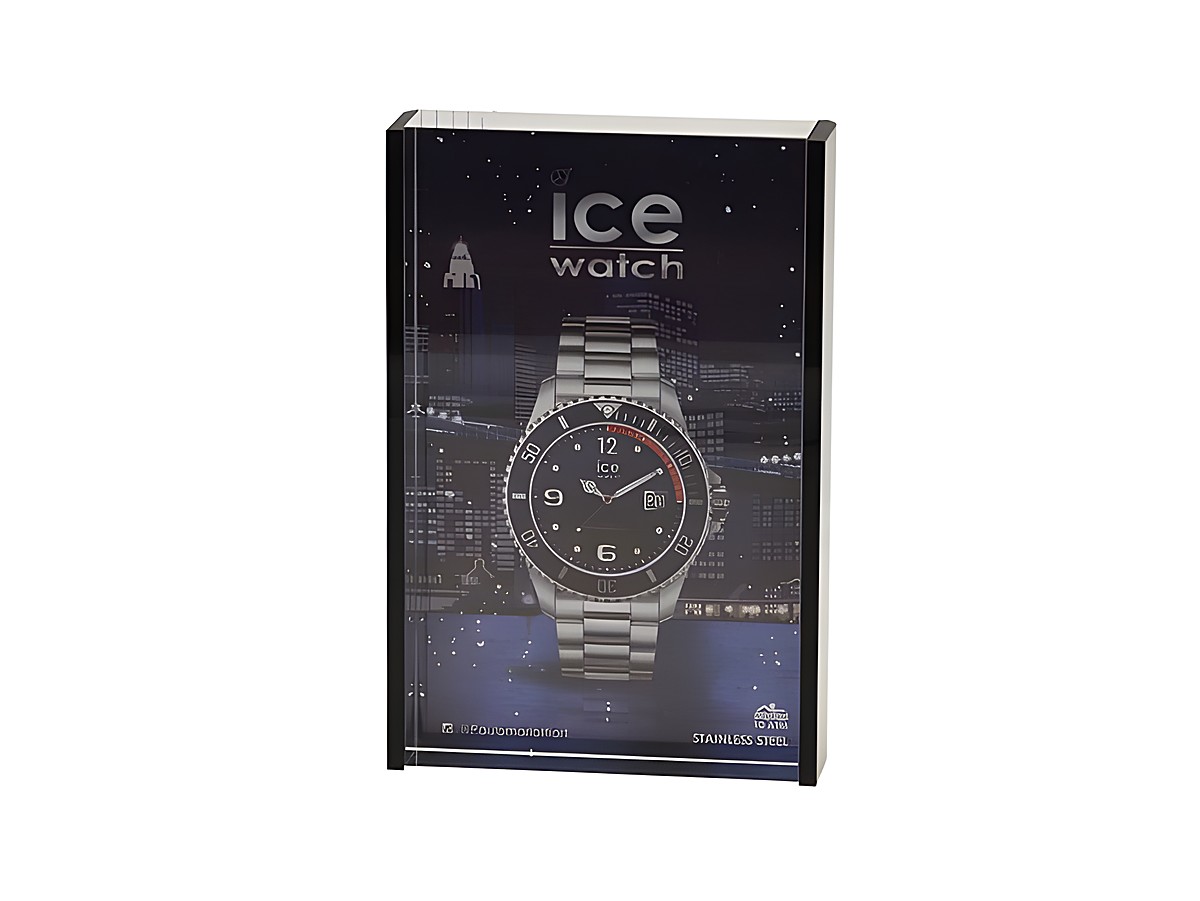 Ein schwarzer Bilderrahmen von Ice Watch zeigt eine stilvolle Armbanduhr mit Edelstahlarmband und schwarzem Ziffernblatt, platziert vor einer nächtlichen Stadtlandschaft.