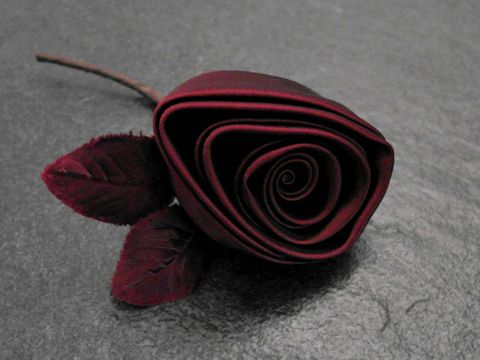 Haarschmuck und Brosche in Form einer bordeauxroten Satinrose mit zarten Blütenblättern und grünen Blättern, hergestellt von Juwelier Harnisch, ideal für edle Anlässe.
