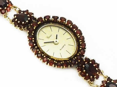 Granat Schmuck Uhr 18 cm mit Blüte aus Gold und Granatschmuck, Hersteller Juwelier Harnisch, verziert mit Stein und Perle, elegantes Design mit ovalem Zifferblatt.