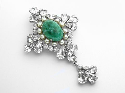 Königliche Strass Brosche -Sexy City Look- von Juwelier Harnisch, präsentiert sich in elegantem Design mit einem ovalen grünen Stein und funkelnden weißen Strasssteinen.