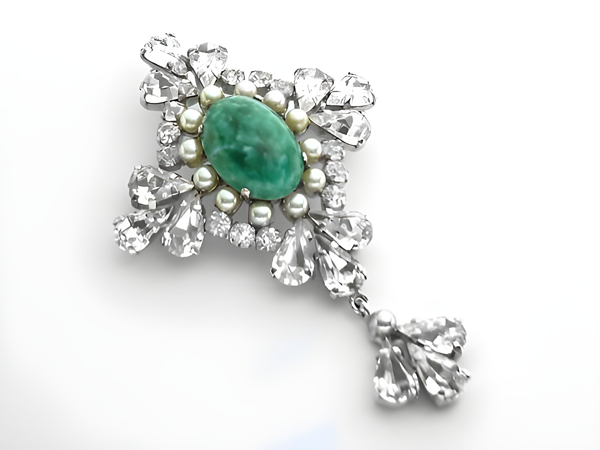 Königliche Strass Brosche -Sexy City Look- von Juwelier Harnisch, präsentiert sich in elegantem Design mit einem ovalen grünen Stein und funkelnden weißen Strasssteinen.