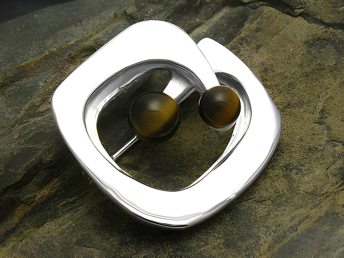 Brosche Design mit Tigerauge echt Silber, Hersteller Juwelier Harnisch, elegante Form mit zwei runden Tigerauge-Steinen, auf einem rustikalen Untergrund präsentiert.