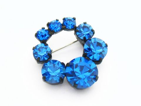 Strass Brosche rund in Blau, gefasst, neu, Hersteller Juwelier Harnisch. Die Brosche zeigt mehrere leuchtend blaue Steine in ansprechender Anordnung.