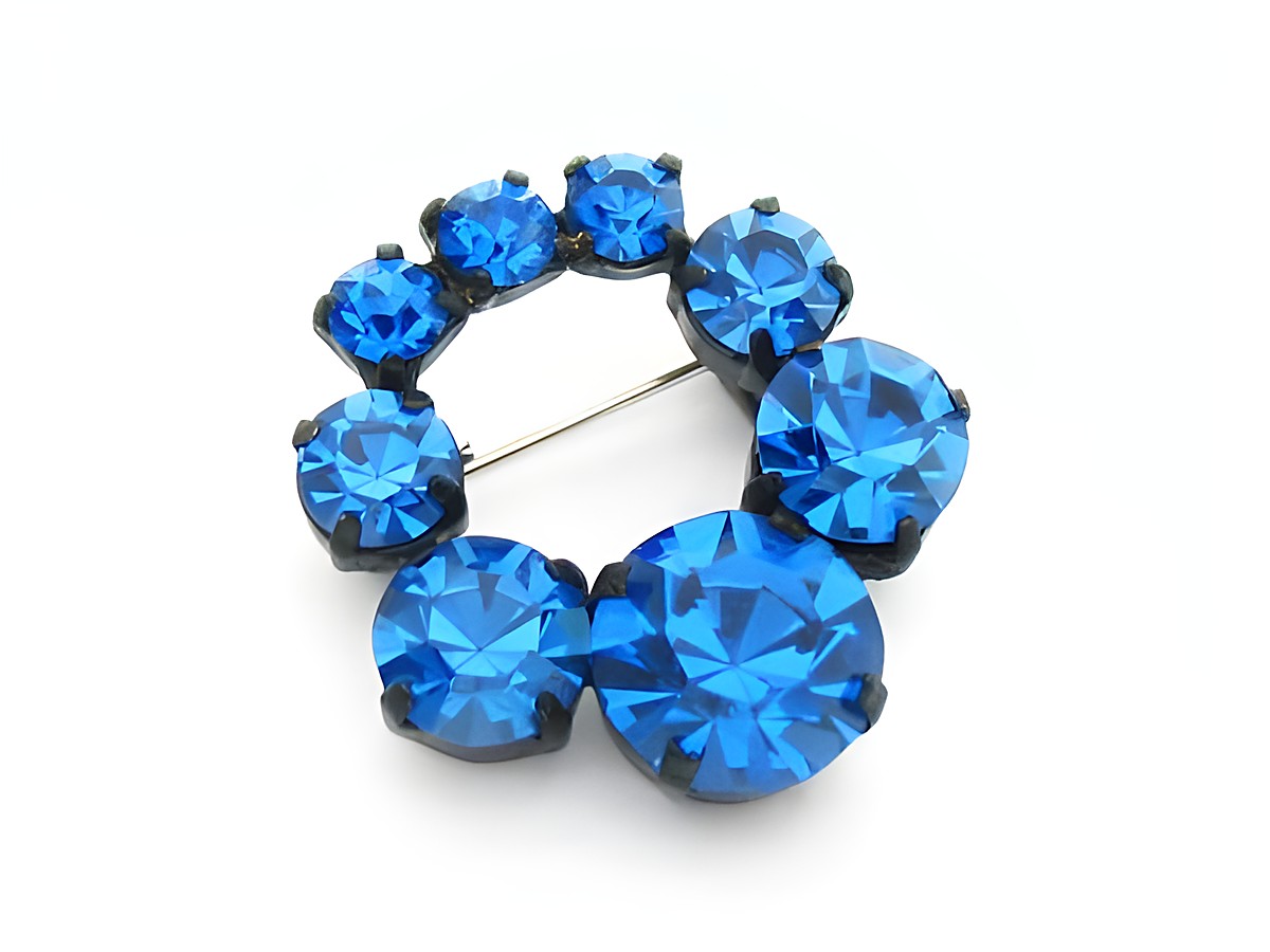Strass Brosche rund in Blau, gefasst, neu, Hersteller Juwelier Harnisch. Die Brosche zeigt mehrere leuchtend blaue Steine in ansprechender Anordnung.