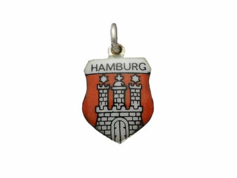 Ein silberner Anhänger mit dem Wappen von Hamburg, darauf abgebildet sind der Türme und das Tor in kräftigen Farben, Hersteller ist Juwelier Harnisch aus Hamburg.