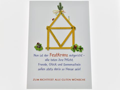 Auf der Grußkarte ist ein Festkranz aus einem Zollstock, umgeben von grünen Pflanzen, einem Marienkäfer und Klee, mit dem Text zum Richtfest und den besten Wünschen.