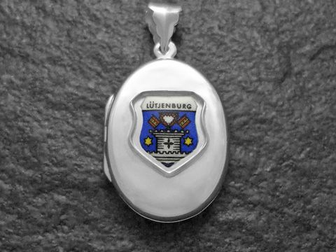 Das Bild zeigt ein silbernes Medaillon mit dem Stadtwappen von Lütjenburg in Schleswig-Holstein. Das Wappen ist farbig mit einer stilisierten Darstellung und befindet sich auf der Vorderseite des Medaillons.