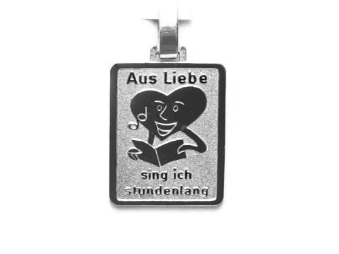 Silber Anhänger mit dem Motiv eines lachenden Gesichts, das eine herzförmige Figur umarmt. Darunter steht der Text Aus Liebe sing ich stundenlang. Hersteller Juwelier Harnisch.