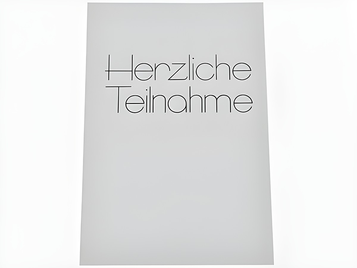 Eine weiße Trauerkarte mit der Schrift "Herzliche Teilnahme" in eleganter, schwarzer Schriftart. Hersteller ist Juwelier Harnisch. Die Karte ist schlicht und würde für Beileidsbekundungen verwendet.