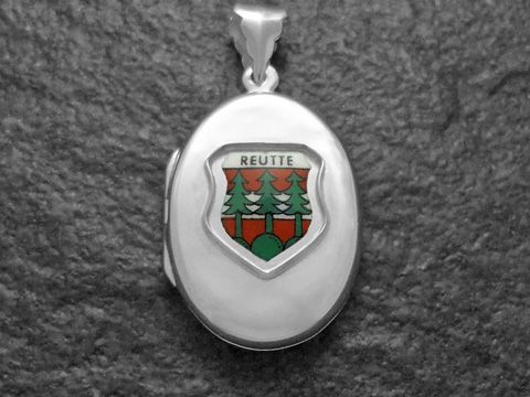 Silbernes Medaillon mit dem Stadtwappen von Reutte, Österreich. Das Wappen zeigt grüne Bäume und rote Elemente, eingefasst in einem ovalen Rahmen. Hersteller ist Juwelier Harnisch.