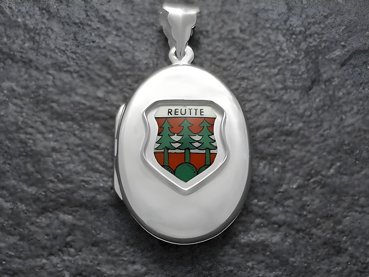 Silbernes Medaillon mit dem Stadtwappen von Reutte, Österreich. Das Wappen zeigt grüne Bäume und rote Elemente, eingefasst in einem ovalen Rahmen. Hersteller ist Juwelier Harnisch.