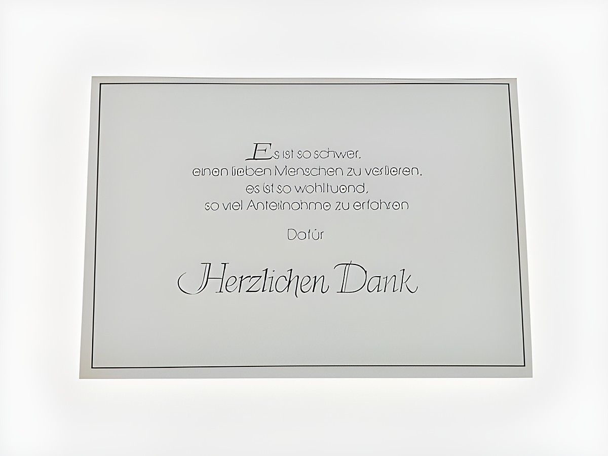Es ist eine Dankeskarte zu sehen, schlicht in weiß mit schwarzer und silberner Schrift, auf der danken für die Anteilnahme anlässlich eines Verlustes ausgedrückt wird.