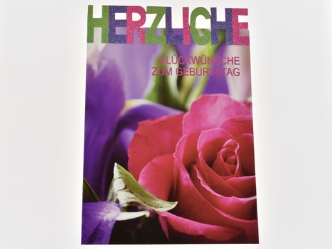 Eine Geburtstagskarte mit bunten Buchstaben, die "Herzliche Glückwünsche zum Geburtstag" sagen, und einer Rosenabbildung in verschiedenen Farben, hergestellt von Juwelier Harnisch.