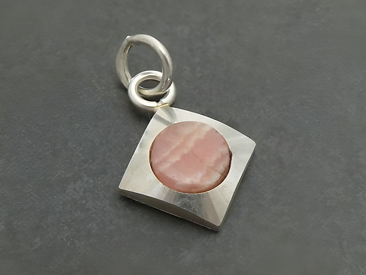 Silber Anhänger rhodiniert mit quadratischem Design und einem runden Rhodochrosit in rosa Farbton, hergestellt von Juwelier Harnisch. Der Anhänger ist feminin und elegant.