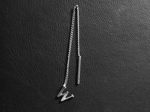 Silber Ohrring mit Buchstabe W als Initialen Ohrhänger, ein einzelnes Stück, hergestellt von Juwelier Harnisch, filigranes Design auf schwarzem Hintergrund.