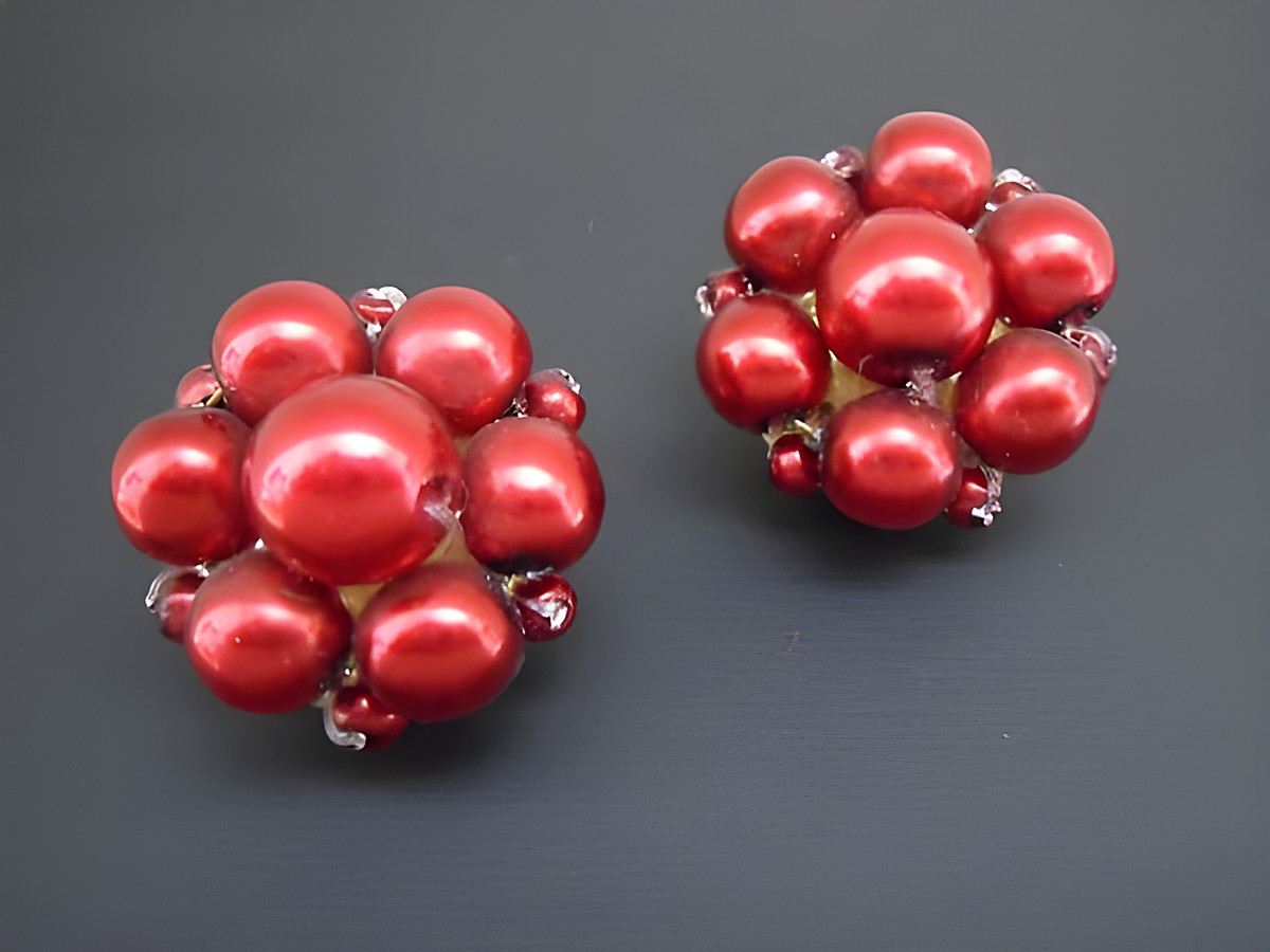 Ohrclip in dunklem Rot mit blumigem Design, ergänzt durch goldfarbene Elemente und synthetische Zuchtperlen, hergestellt von Juwelier Harnisch.