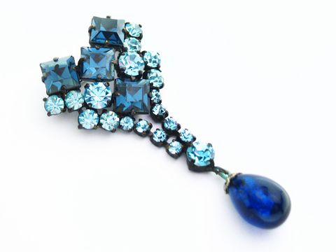 Blaue Strass Damen Brosche im sexy City Look von Juwelier Harnisch, verziert mit verschiedenen blauen Strasssteinen und einem hängenden, blauen Tropfen. Ideal für stilvolle Akzente.