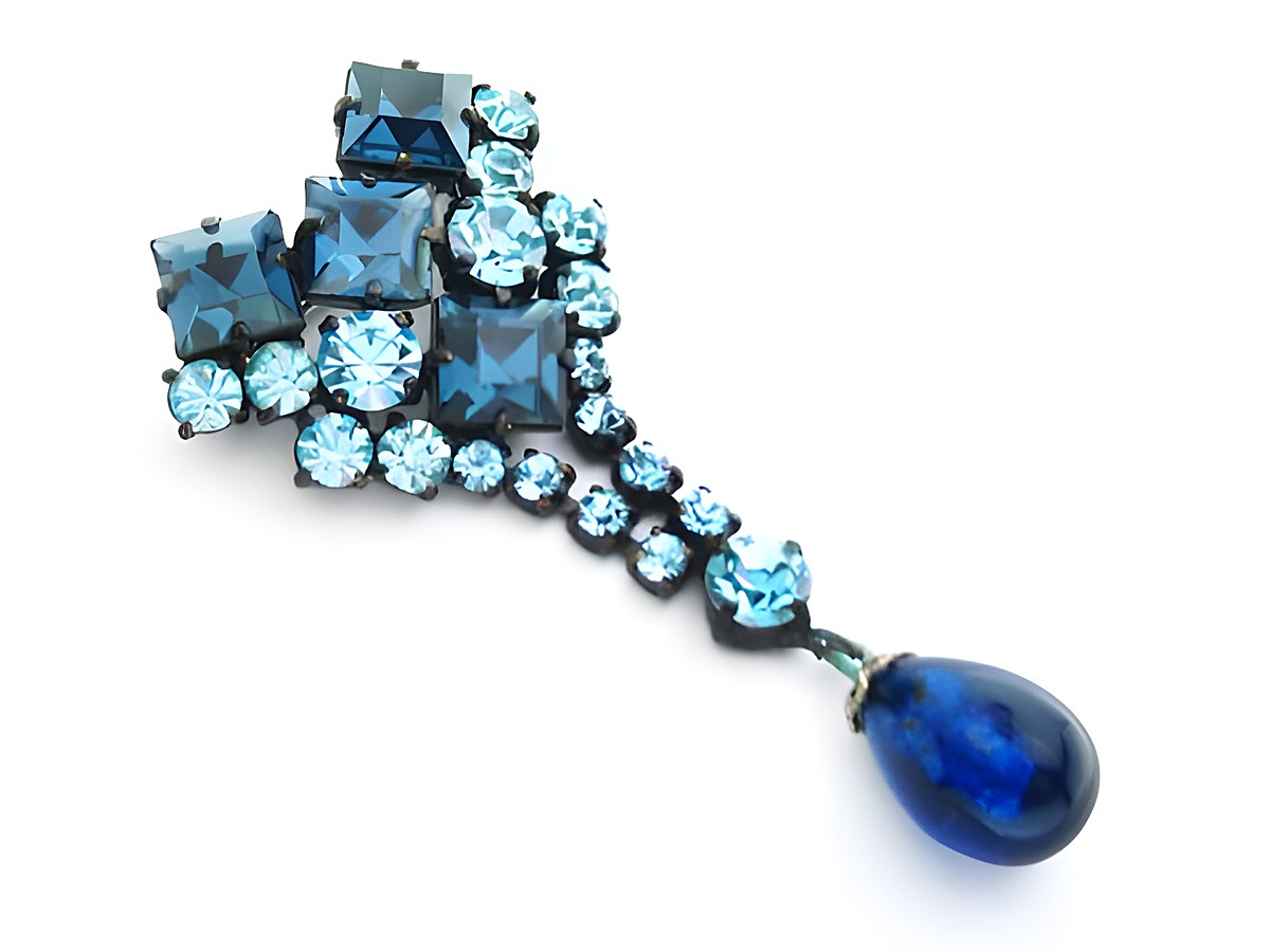 Blaue Strass Damen Brosche im sexy City Look von Juwelier Harnisch, verziert mit verschiedenen blauen Strasssteinen und einem hängenden, blauen Tropfen. Ideal für stilvolle Akzente.