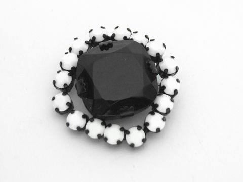 Strass Brosche in Weiß und Schwarz, rundlich gefasst, mit einem zentralen schwarzen Stein und umliegenden weißen Strasssteinen, Hersteller Juwelier Harnisch, elegant und zeitlos.