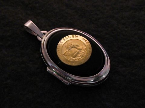 Ein elegantes Medaillon aus Weißgold 585 mit einem ovalen Cabochon in Schwarz, der eine goldene Münze zeigt. Der Hersteller ist Juwelier Harnisch.