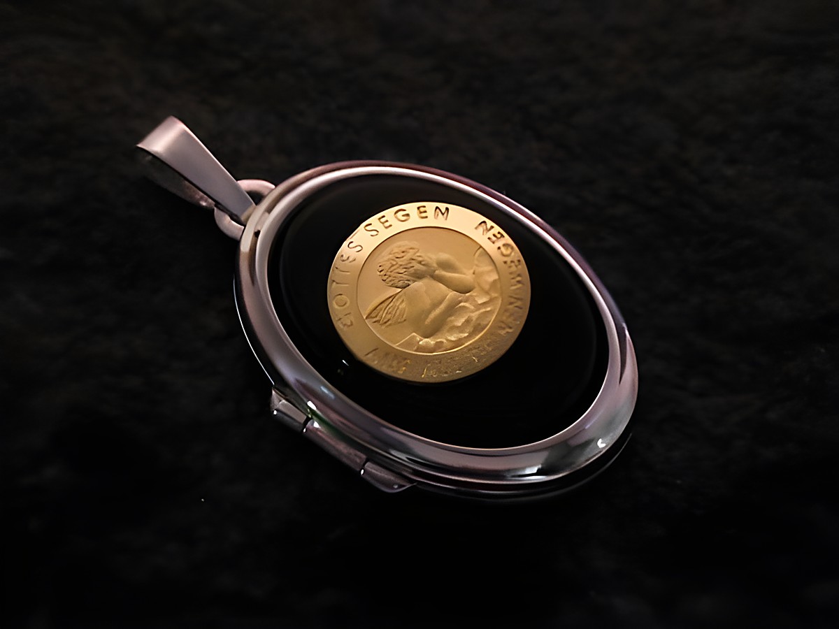 Ein elegantes Medaillon aus Weißgold 585 mit einem ovalen Cabochon in Schwarz, der eine goldene Münze zeigt. Der Hersteller ist Juwelier Harnisch.