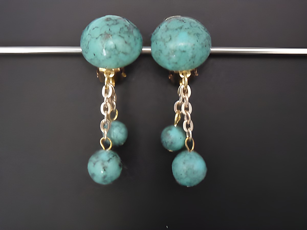 Ohrclip in zeitlosem Design mit türkisfarbenem Kunstharz und goldfarbener Kette, Hersteller Juwelier Harnisch, elegant und auffällig, ideal für besondere Anlässe.