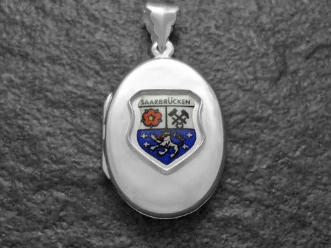 Silbernes Medaillon mit dem Stadtwappen von Saarbrücken, Deutschland. Das Wappen zeigt als zentrale Elemente eine Blume und zwei gekreuzte Schlägel, umgeben von einem blauen Schild.