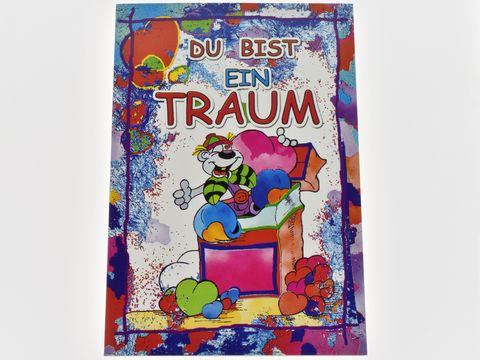 Eine bunte Grußkarte mit der Aufschrift "DU BIST EIN TRAUM". Auf der Karte sitzt eine Lümmel-Figur auf einer Geschenkbox umgeben von Herzen und bunten Formen, Hersteller: Juwelier Harnisch.