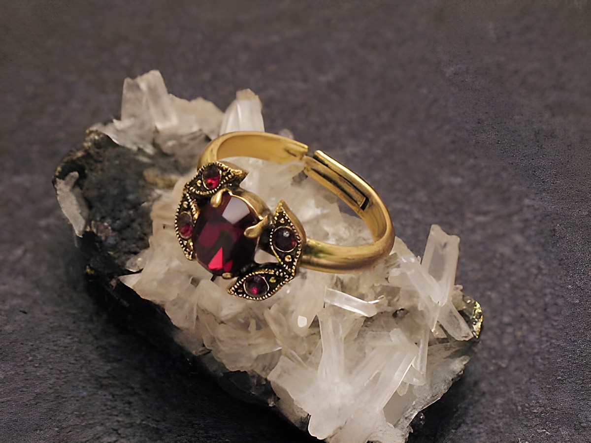 Modeschmuck Ring mit Granat Imitation aus Strass, gefertigt von Juwelier Harnisch, mit goldfarbenem Band und dekorativen Steinbesätzen, auf Mineralien-Basis präsentiert.