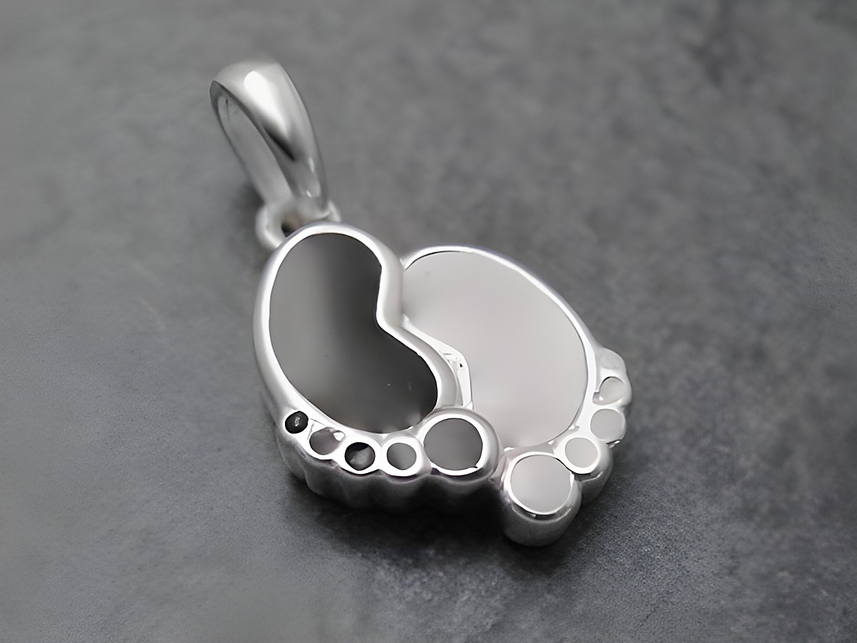 Ein niedlicher Anhänger in Form von Babyfußabdrücken aus Sterling Silber in Schwarz und Weiß, ideal als Schmuckstück für Kinder, hergestellt von Juwelier Harnisch.