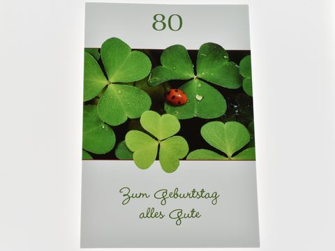 Eine Geburtstagskarte mit der Aufschrift 80, verziert mit Glücksklee und einem Marienkäfer, darunter steht Zum Geburtstag alles Gute, Hersteller Juwelier Harnisch.