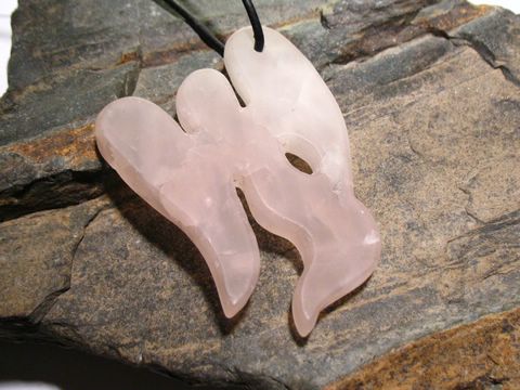 37070-0 Engel Umriss in Rosenquarz mit einer Größe von 5 cm, an einer Lederkette befestigt, präsentiert auf einer natürlichen Steinoberfläche, hergestellt von Juwelier Harnisch.