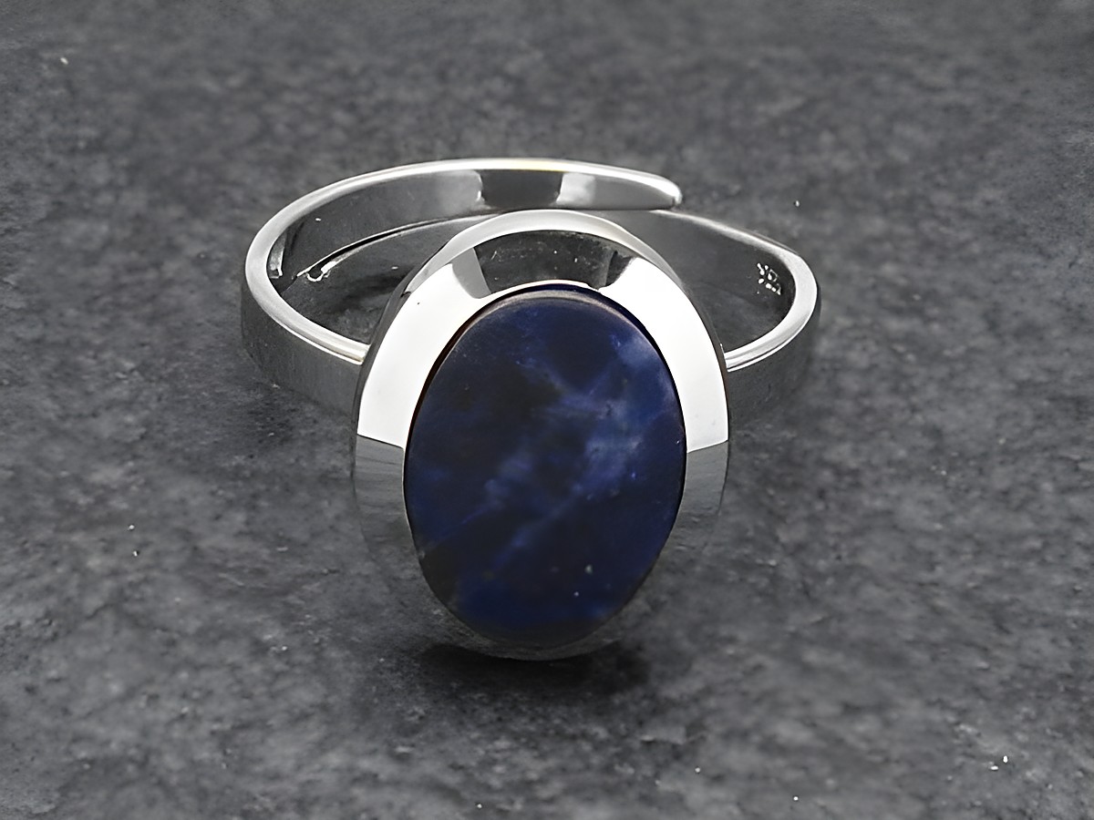 Silberring rho in ovaler Form, verstellbar, mit blauem Sodalithstein, rhodiniert, Hersteller Juwelier Harnisch auf schwarzem Untergrund.